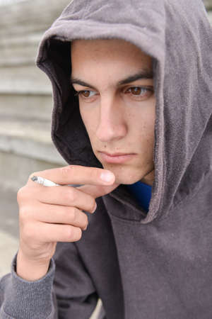 Young man in depression smoking a cigarette on a stadion. Concept of young people with harmful habitsの写真素材
