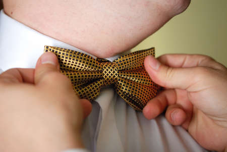 groomsmen helping groom to put on bow tieの写真素材