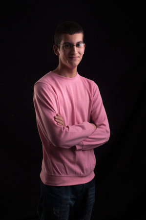Young man with glasses standing with arms crossed on black backgroundの写真素材