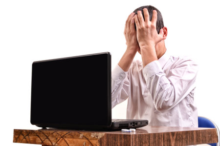 Frustrated young man, holding his head in front of a laptop in the classroom