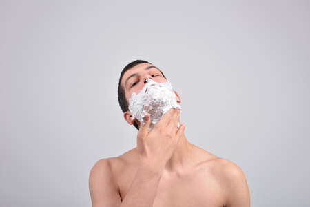 Closeup of a young man preparing to shave, he puts foam on his cheekの写真素材