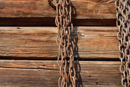 Rusty chain hanging on old wooden wallの写真素材