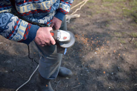 Close up of a man sharpen an ax using electric grinder. Sparks while grinding iron. Selective focusの写真素材