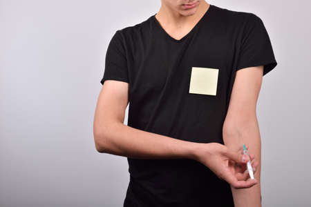 Hand with heroin syringe with blank post it. The concept of not starting to use drugsの写真素材