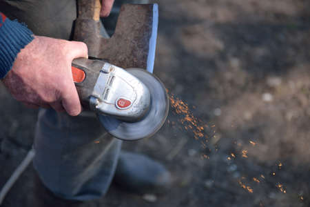 Close up of a man sharpen an ax using electric grinder. Sparks while grinding iron. Selective focusの写真素材
