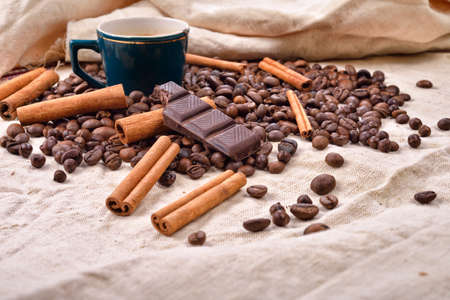 Cup of hot coffee with cinnamon sticks, bitten bar of chocolate on vintage texture background, selective focusの写真素材