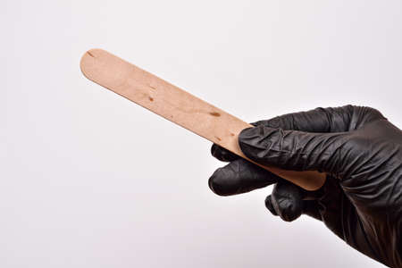 A beauticians hand with black glove holding a spatula for wax, preparing for epilation, on whiteの写真素材