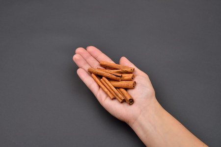 Hand of a woman holding a pile of cinnamon pods isolated on black background. Spice. Taste. Cooking. Food and beverage flavoringの写真素材