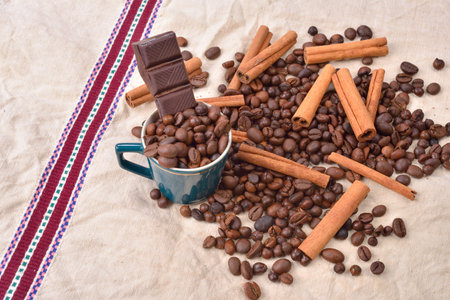 Cup of coffee with cinnamon sticks, bar of chocolate on vintage texture. Roasted coffee beans on...
