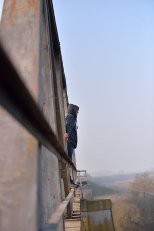 Sad young man standing on the edge of a bridge. Looking away thinking. Depression conceptの写真素材