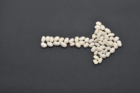 Arrow made from white beans, pointing the way on black background. Food vegan, vegetarian. Healthy foodの写真素材