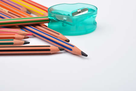 Picture of some pencils with stripes of different colors and a green pencil put in a pencil sharpener on a white background.の写真素材