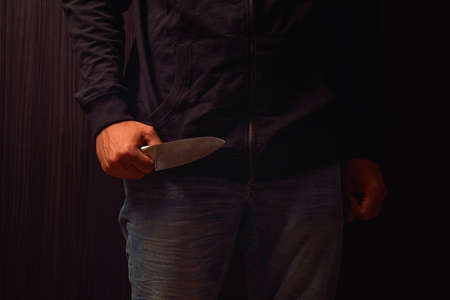 Closeup of a young man hand, holding a knife, about to attack, over black background. Representing the concept of danger, stress, unfulfillment, risk. Lights and shadowsの写真素材
