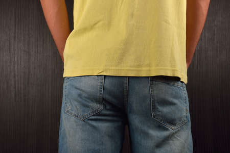 Back of young man wearing yellow blank t-shirt, standing in a studio on dark background. Picture halved. Clothing design conceptの写真素材