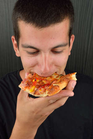 Portrait of a greedy young man eating pizza on a dark background. Fast food, unhealthyの写真素材