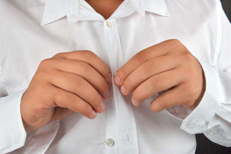 Young man buttoning his white shirt on a dark background. He is dressing in the morning. Clothes detail. Lights and shadowsの写真素材