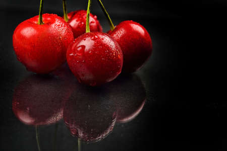 Three red wet cherries against reflective black background in studio. Selective focus. Lights and shadowsの写真素材