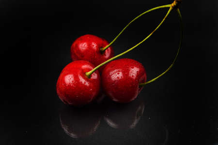 Three red cherries with water drops against reflective black background. Selective focus. Lights and shadows. Healthy and sweet foodの写真素材