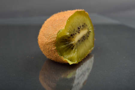 Close up of a half of kiwi which was bitten with teeth with wizened skin on dark reflection background. Natural organic vegetarian food. Healthy snackの写真素材