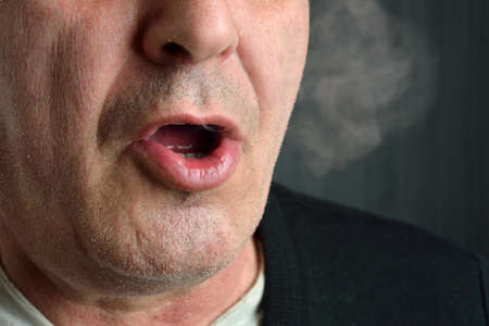 Man smokes cigarette and and releases smoke in a studio - photography of unhealthy addiction. Lifestyle and health. Lights and shadowsの写真素材