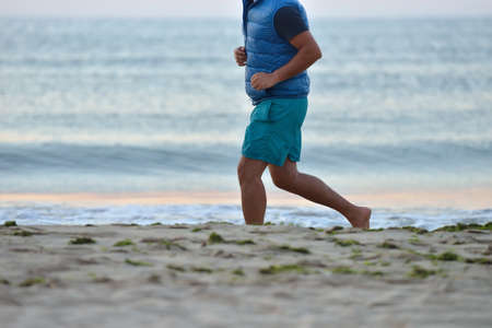 Silhouette of active adult man running and exercising on the beach early in the morning, at the sunrise. Calm water. Healthy lifestyle.の写真素材
