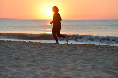 Silhouette of a young girl running alone along the beach of the sea during an amazing sunrise. Concept of sport and freedom. Healthy trainingの写真素材