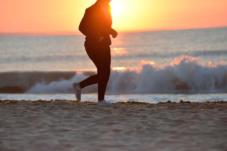 Silhouette of a young girl running alone along the beach of the sea during an amazing sunrise. Concept of sport and freedom. Healthy trainingの写真素材