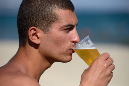 Young handsome sporty man drinking beer at the beach in summertime - relaxing, summer, thirsty...