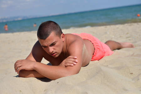 Young man lying on the sand in the sun to tan. Relaxing on vacation, enjoy the beach. Black Sea in the backgroundの写真素材