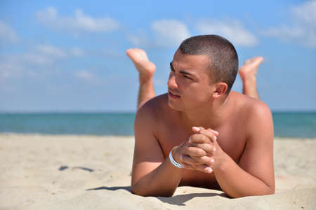Man on beach lying in sand looking to side. Young male enjoying summer travel holiday resting on the beach by the sea. Sunbathの写真素材