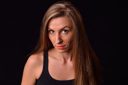 Beautiful blonde young woman in a black undershirt posing in a studio. Look confident and sexy
