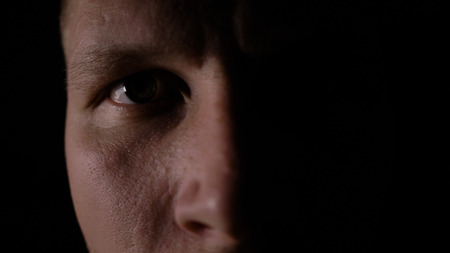 A man looks at the camera in the dark. Close-up eye. Only half of the face is highlighted.の写真素材