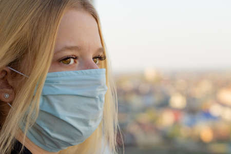 Young woman portrait with medical mask, blurred city background. Concept covid-19 prevention global coronavirus pandemicの写真素材