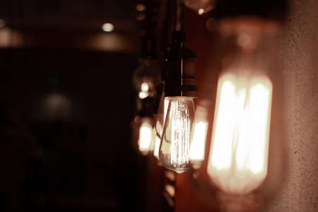 Shining antique Edison style bulbs in the dark. Lighting decor concept. Vintage sepia color light bulb. Blur background of retro lightsの写真素材