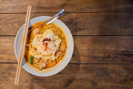 Top view of tom yum noodles with minced pork and fried egg on wooden tableの写真素材