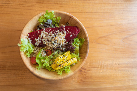 Fresh vegetables and fruits salad with corn, beetroot, millet, lettuce, tomato in wooden bowl on wooden table.の写真素材