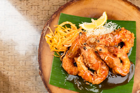 Deep fried prawns with tamarind sauce on banana leaf and wooden plate with sliced egg, fried noodles and lime.の写真素材