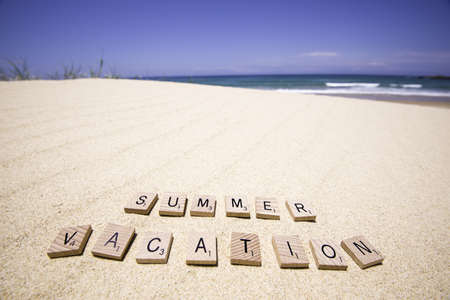 Wooden scrabble tiles laying on white beach, blue sky and rolling waves in the background のeditorial素材