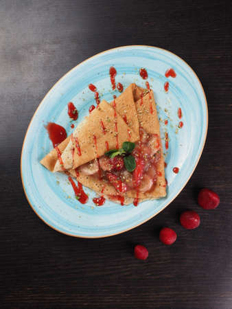 Pancakes pancakes with slices of strawberry and banana in a sweet sauce in a plate on the tableの写真素材
