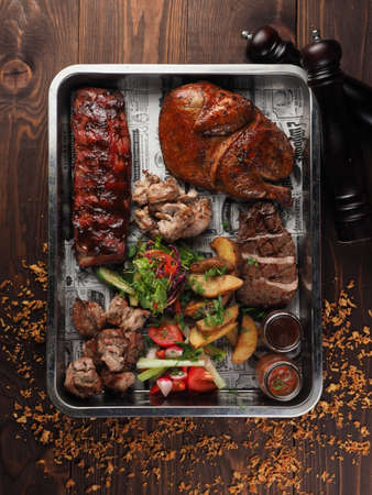 Assorted delicious grilled meat and vegetables with fresh salad and bbq sauce on cutting board on wooden background close up. Big set of Hot Meat Dishesの写真素材