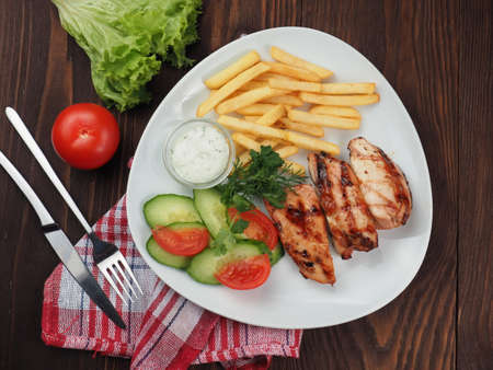 Grilled steaks, french fries and vegetable salad on a plate and rustic backgroundの写真素材