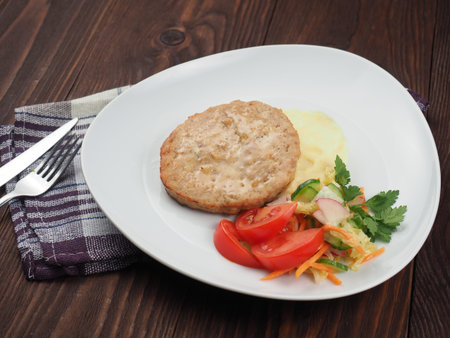 Chicken cutlet with mashed potatoes and vegetables on a plate and rustic background