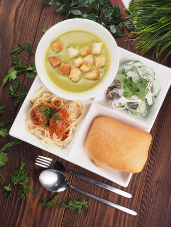 Bento set of Spaghetti and meatballs in tomato sauce, soup with crackers, vegetable salad and bun