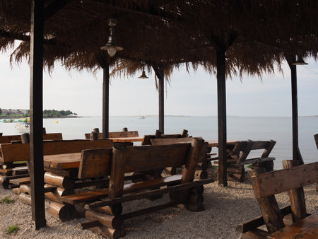 Wooden tables and chairs in a cafe on the beach with the sea in the backgroundの写真素材