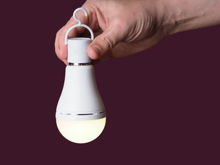 A switched-on LED rechargeable lamp in the hands of a person on a burgundy background