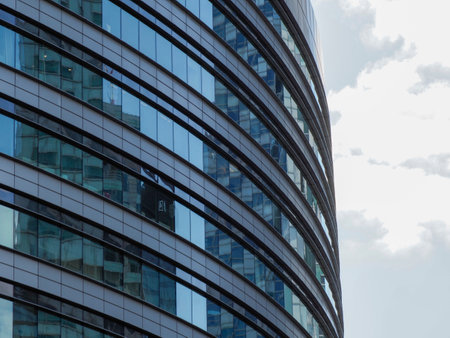 Curved Blue Glass Facade of Contemporary Office Building with Smooth Reflections in Business Districtの写真素材