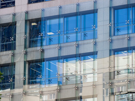Modern Office Building with Clean Glass Facade Reflecting Clear Blue Sky and Surrounding Urban...