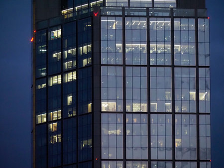 Illuminated glass office tower with grid pattern facade at twilight showcasing modern corporate...