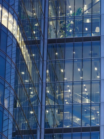 Abstract Blue Glass Facade of Modern Skyscraper with Geometric Reflections and Illuminated Windows...