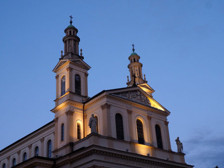 Dramatic upward view of baroque church towers illuminated against evening blue sky showcasing historical architecture in Warsawの写真素材